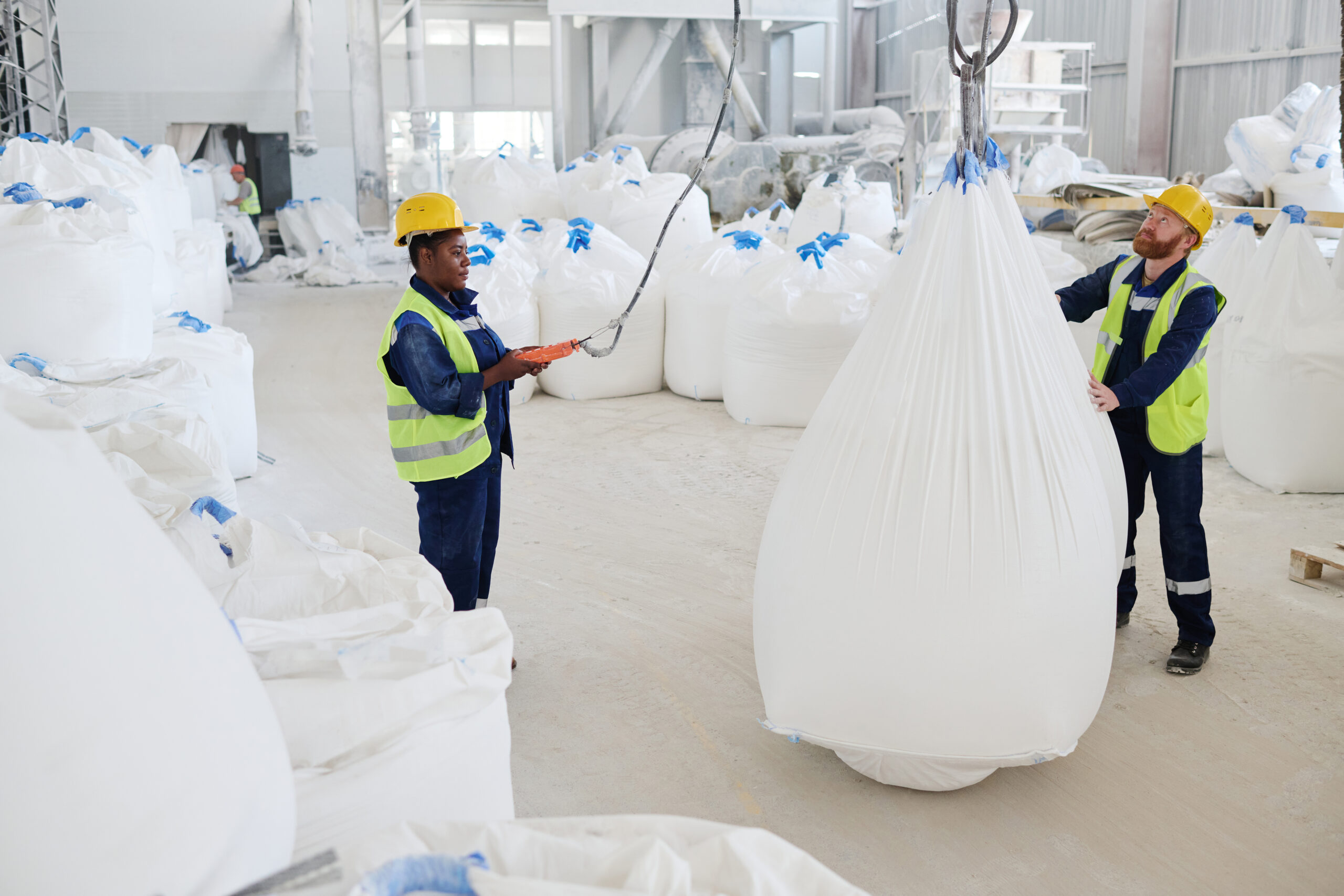 Young male worker helping his female colleague with remote control switch lift huge heavy sack with raw materials in workshop